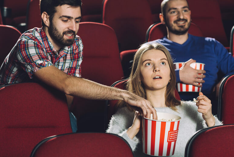 Image of people at a threatre with a guy stealing a girls popcorm